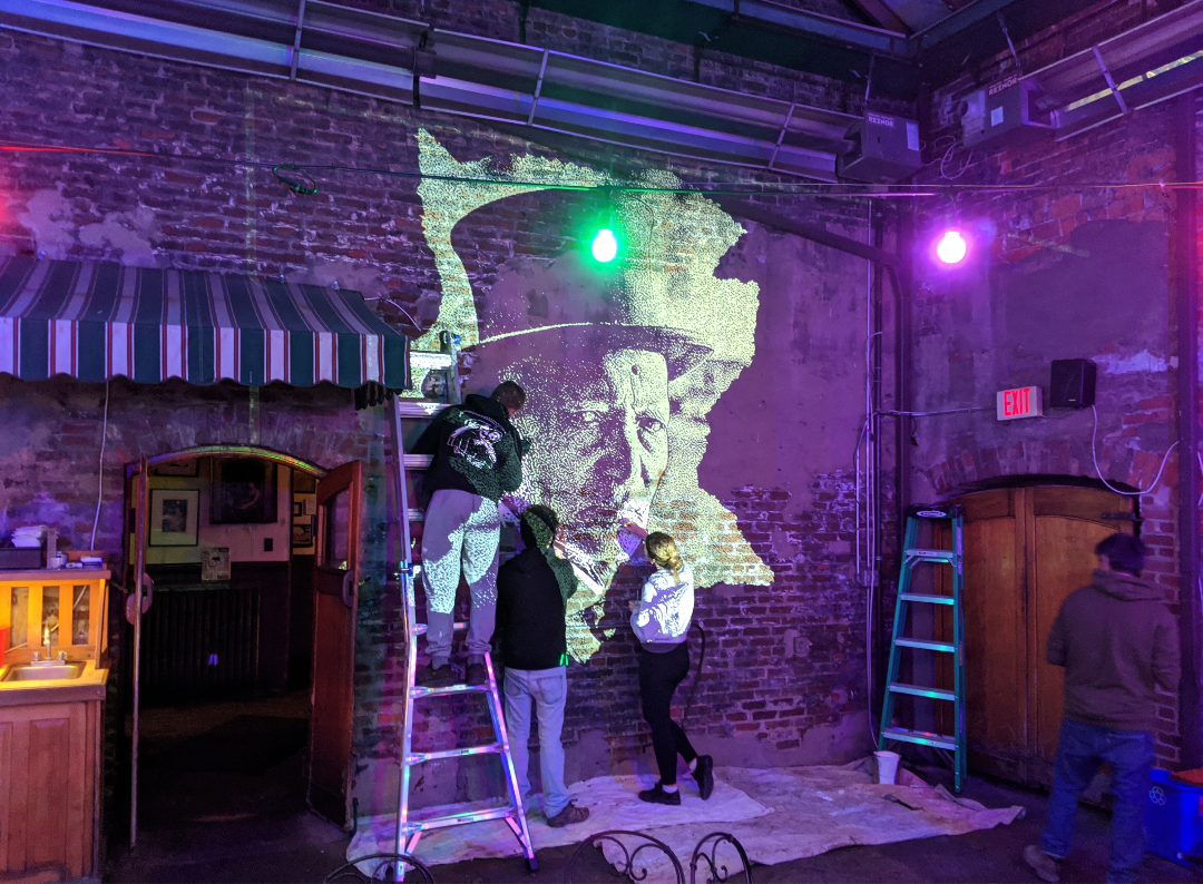 An artist painting a large portrait mural on exposed brick at Arnold's Bar and Grill in Cincinnati.