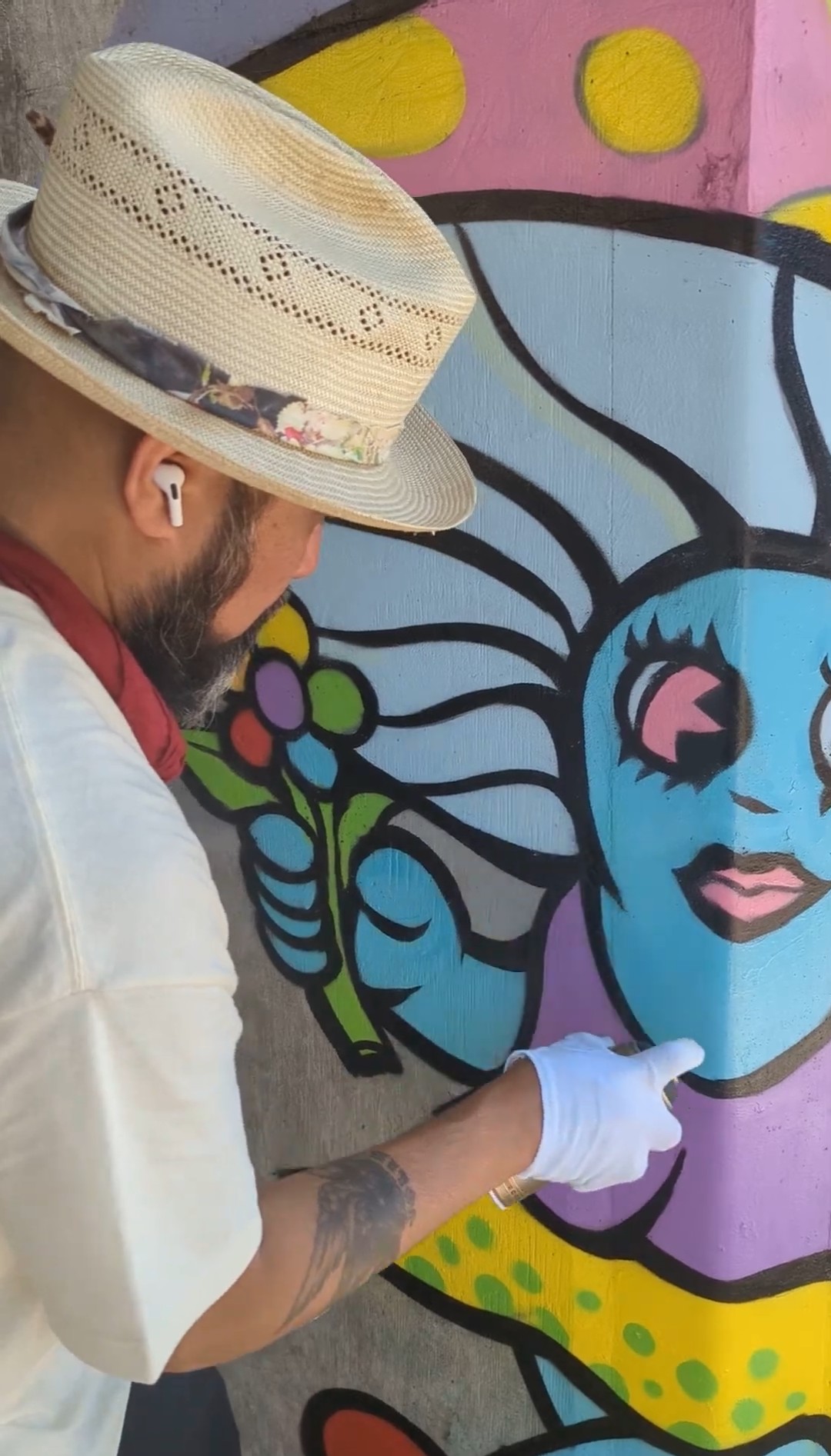 Close-up of an artist's hand painting fine detail on a mural of a character with flowing hair.