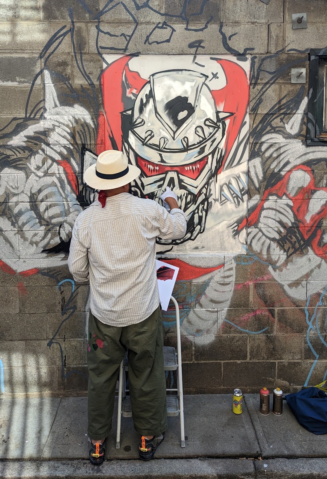 Artist painting a large-scale mural on an exterior brick wall.